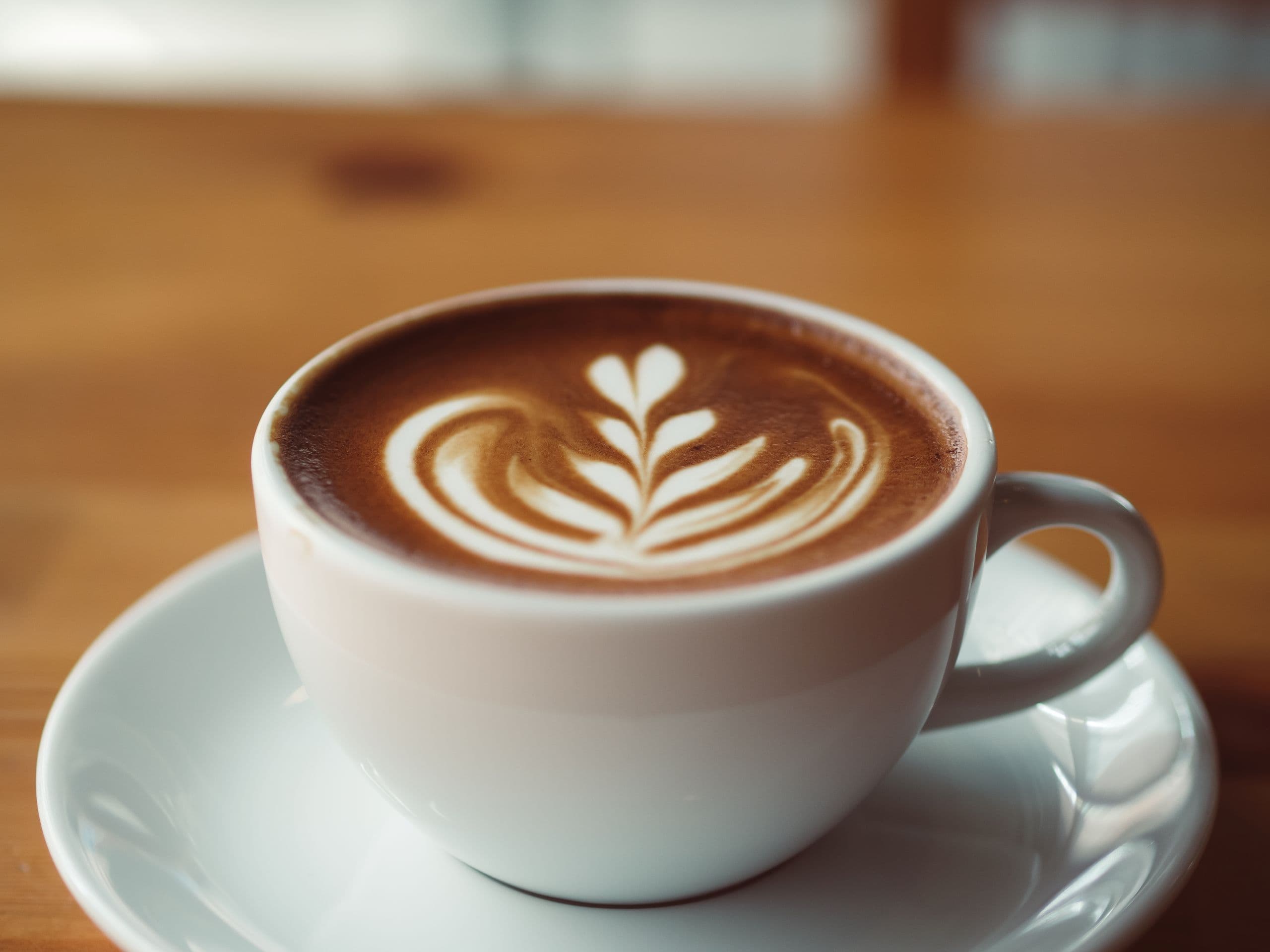 A ceramic cup of coffee with roasted beans and ripe coffee cherries